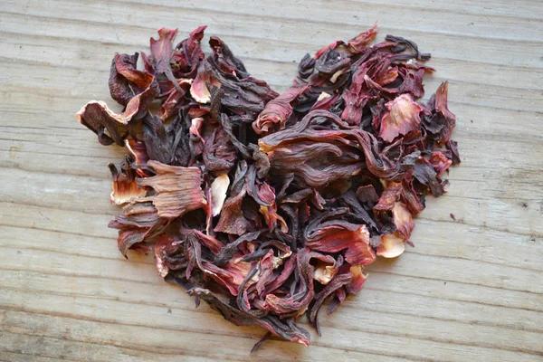 Dry leaves and petals of hibiscus tea in a shape of heart on wooden table — Stock Photo, Image
