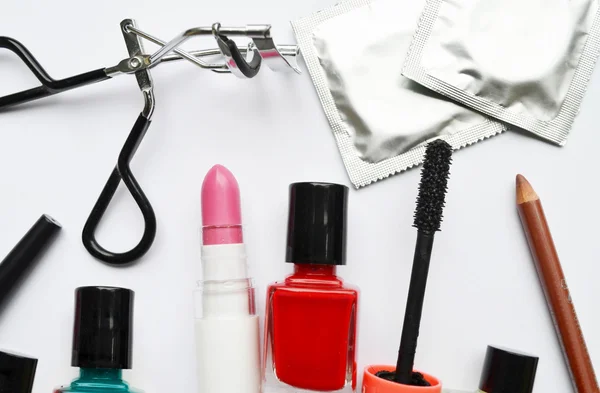 Couple of condoms and a cosmetics set with black mascara, pink and red nail polish and lipstick and eyelash curler isolated on white — Stock Photo, Image