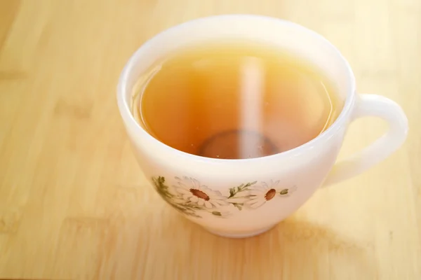 Kamillentee in einer weißen Vintage-Tasse mit Gänseblümchen auf Holztisch — Stockfoto