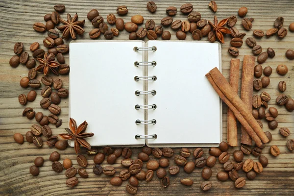 Un cuaderno en espiral retro vacío con muchos granos de café tostados, estrellas de anís picantes y palitos de canela — Foto de Stock