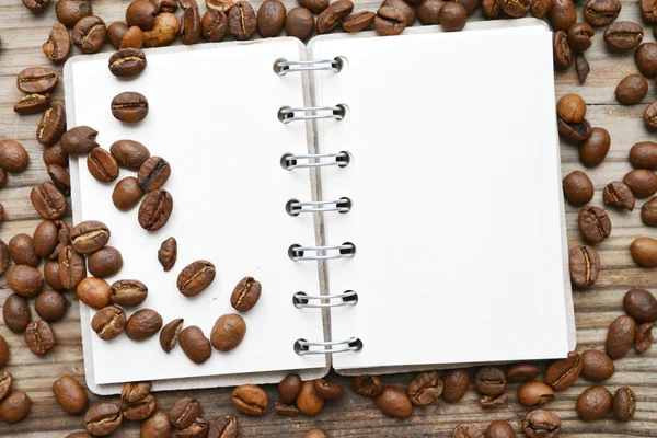 Un carnet spirale rétro vide avec beaucoup de grains de café torréfiés — Photo