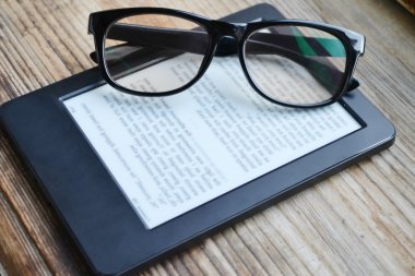 Black ereader with retro glasses on wooden table clipart