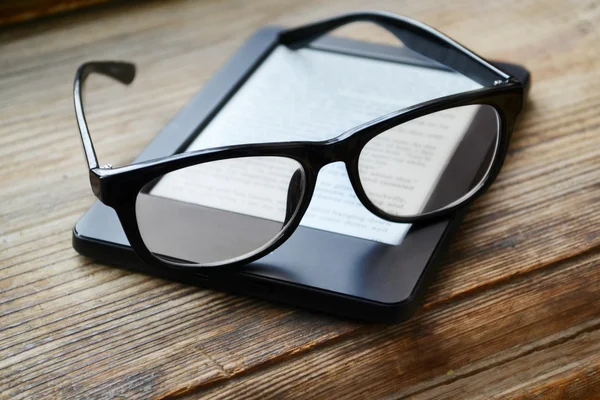 Black ereader with retro glasses on wooden table — Stock Photo, Image