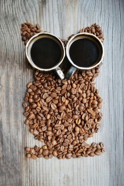 Un montón de granos de café tostados y tazas de café en forma de búho — Foto de Stock