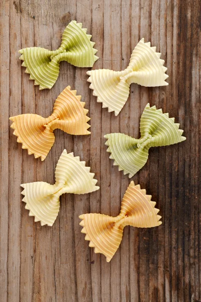 Borboleta não cozida em forma de farfalle de macarrão colorido na mesa de madeira — Fotografia de Stock