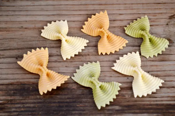 Borboleta não cozida em forma de farfalle de macarrão colorido na mesa de madeira — Fotografia de Stock