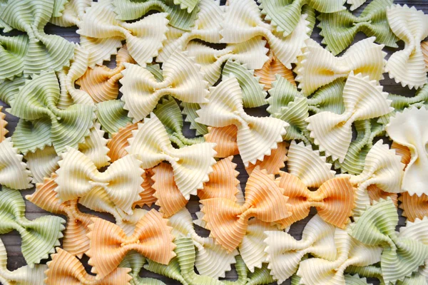Ungekochte Schmetterlingsform bunte Pasta Farfalle auf Holztisch — Stockfoto