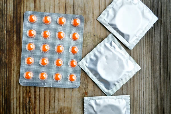 3 prezerwatywy i pomarańczowy tabletki antykoncepcyjne na drewnianym stole — Zdjęcie stockowe