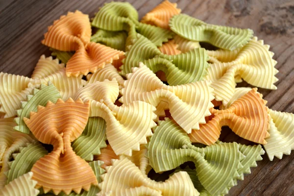 Borboleta não cozida em forma de farfalle de macarrão colorido na mesa de madeira — Fotografia de Stock