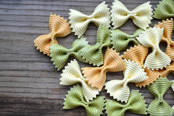 Ungekochte Schmetterlingsform bunte Pasta Farfalle auf Holztisch — Stockfoto