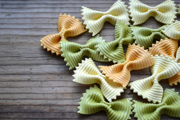 Borboleta não cozida em forma de farfalle de macarrão colorido na mesa de madeira — Fotografia de Stock