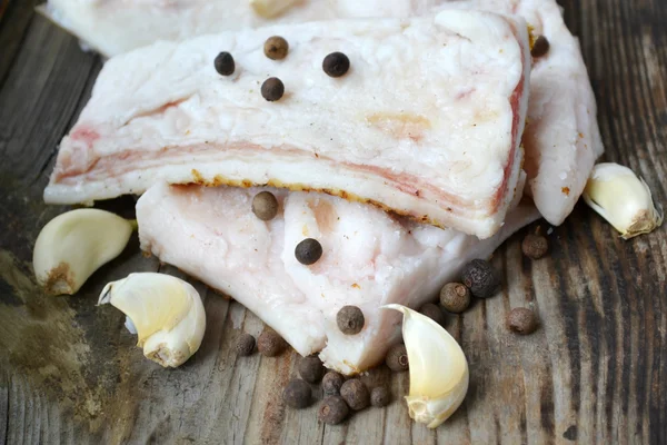 White pork fat called salo with garlic and pepper on wooden kitchen table