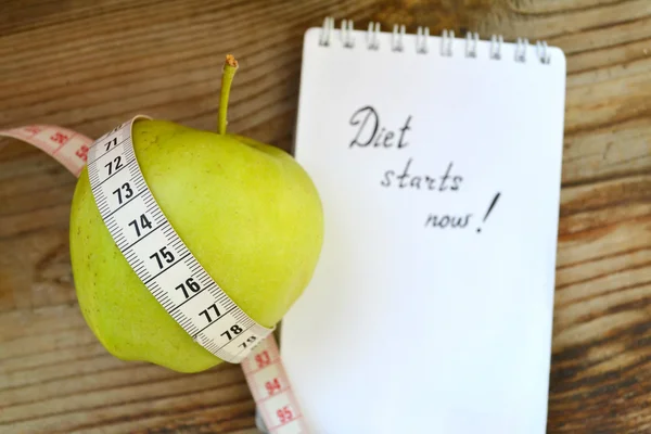 Diet concept with green apple, a notebook and a measuring tape on wooden table — Stock Photo, Image