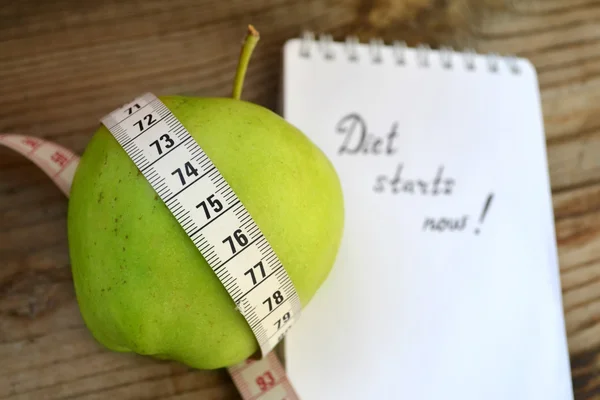 Yeşil elma, bir not defteri ve ahşap masa üzerinde bir ölçüm bandı ile diyet kavramı — Stok fotoğraf