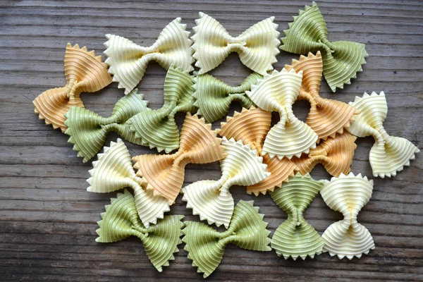 Borboleta não cozida em forma de farfalle de macarrão colorido na mesa de madeira — Fotografia de Stock