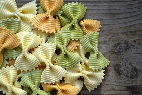 Ungekochte Schmetterlingsform bunte Pasta Farfalle auf Holztisch — Stockfoto