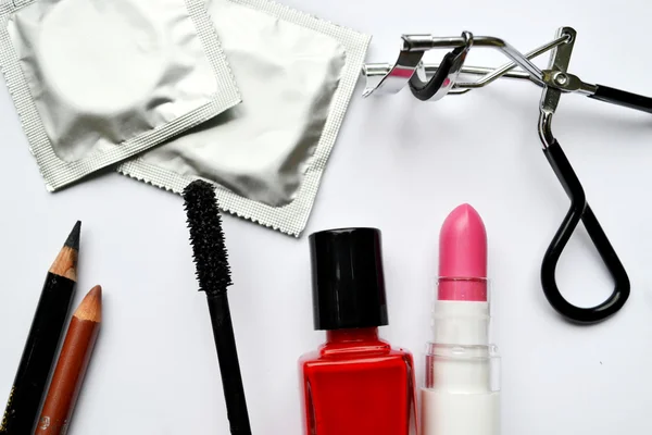 Ein paar Kondome und ein Kosmetik-Set mit schwarzer Mascara, rosa und rotem Nagellack sowie Lippenstift und Wimpernzange isoliert auf weiß — Stockfoto