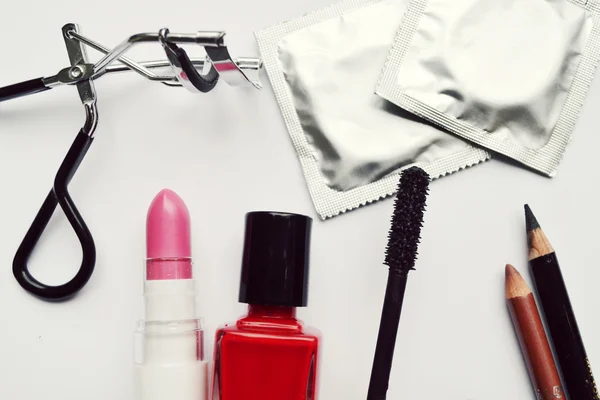 Paar van condooms en een cosmetica bezet met zwarte mascara, roze en rood nagellak en lippenstift en wimper krultang geïsoleerd op wit — Stockfoto