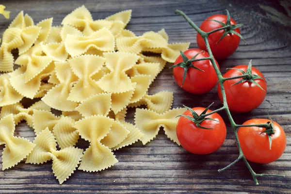 Mazzo di pomodorini rossi e farfalle di pasta a forma di farfalle sul tavolo di legno — Foto Stock