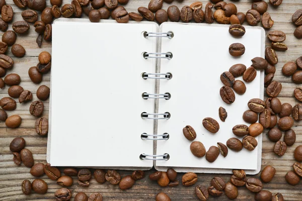 An empty retro spiral notebook with lots of roasted coffee beans — Stock Photo, Image