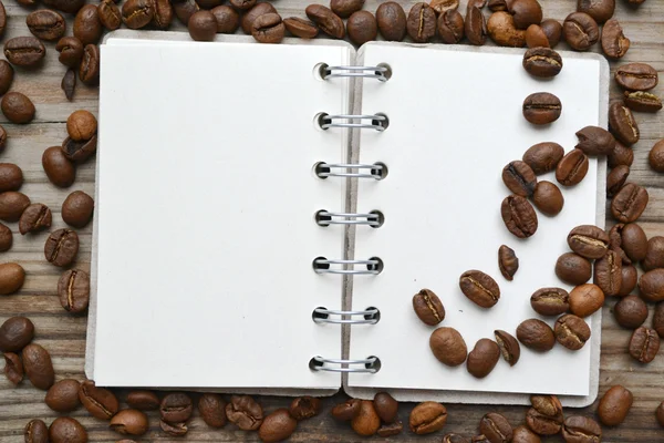 An empty retro spiral notebook with lots of roasted coffee beans — Stock Photo, Image