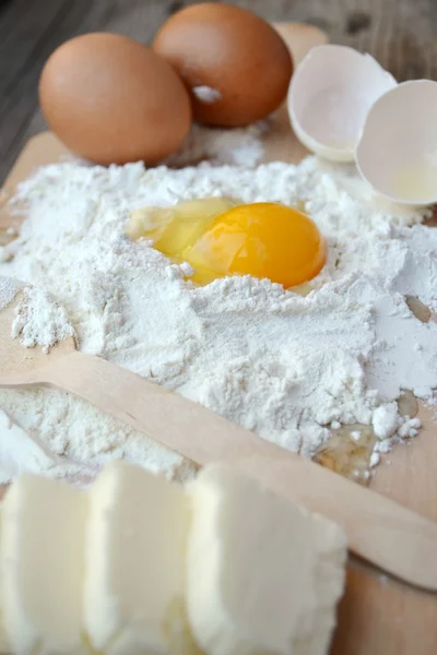 Farine blanche avec œufs, beurre et cuillère en bois sur une plaque de cuisson — Photo