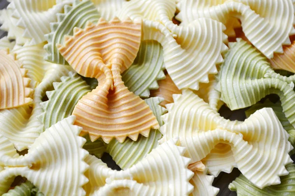 Borboleta não cozida em forma de farfalle de macarrão colorido na mesa de madeira — Fotografia de Stock