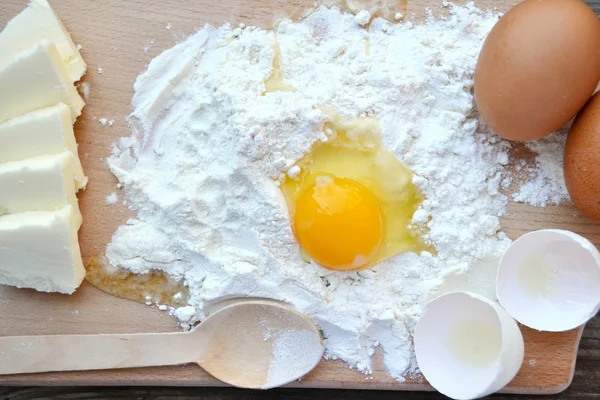 White flour with eggs, butter and wooden spoon on a cooking board — Stock Photo, Image