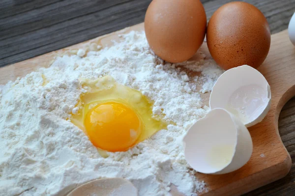 White flour with eggs, butter and wooden spoon on a cooking board — Stock Photo, Image