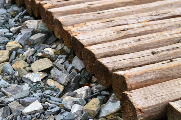 Lots of little gray pebble stones with a pile of firewood logs and blocks — Stock Photo, Image