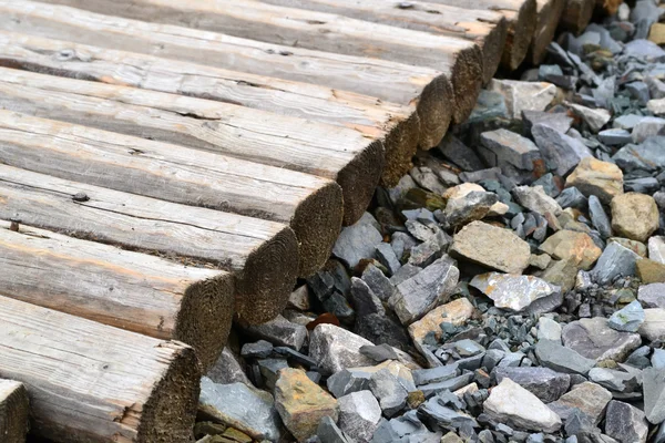 Lots of little gray pebble stones with a pile of firewood logs and blocks — Stock Photo, Image