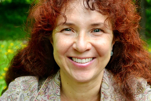 Mujer hermosa feliz con el pelo rojo en sus cuarentas oliendo al aire libre — Foto de Stock