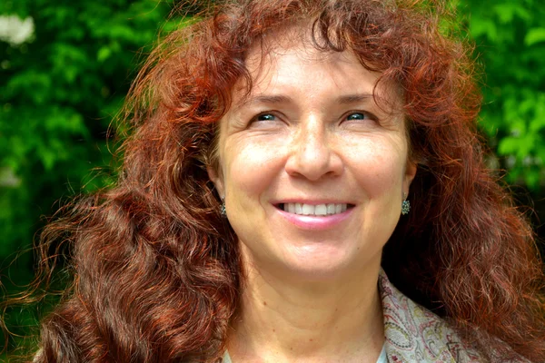 Mujer hermosa feliz con el pelo rojo en sus cuarentas oliendo al aire libre — Foto de Stock