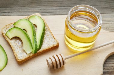 Altın bal honeystick ve ahşap tahta üzerinde yeşil avokado ile sağlıklı bir sandviç ile