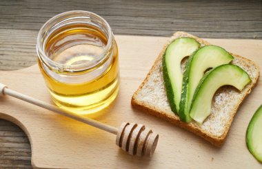 Altın bal honeystick ve ahşap tahta üzerinde yeşil avokado ile sağlıklı bir sandviç ile