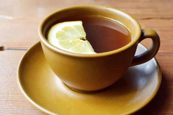 Коричневая чашка травяного чая с ломтиком лимона на деревянном столе — стоковое фото