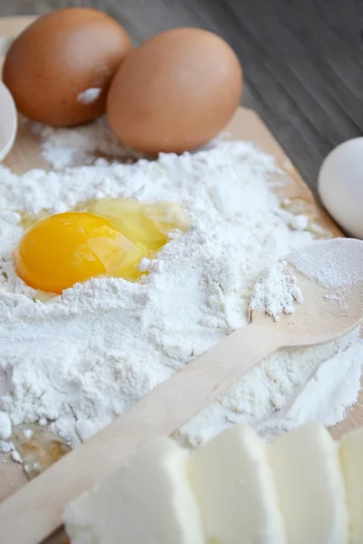 White flour with eggs, butter and wooden spoon on a cooking board — Stock Photo, Image