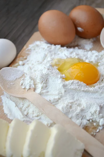 White flour with eggs, butter and wooden spoon on a cooking board — Stock Photo, Image