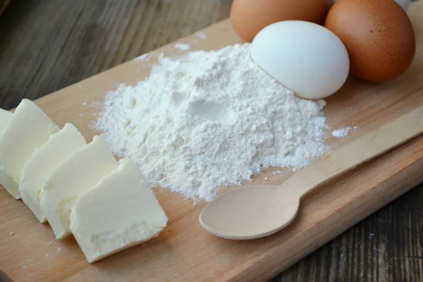 White flour with eggs, butter and wooden spoon on a cooking board — Stock Photo, Image