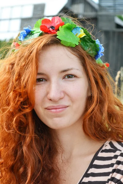 Belle jeune rousse avec des fleurs dans ses cheveux femme souriant joyeusement avec un moulin à l'arrière-plan — Photo