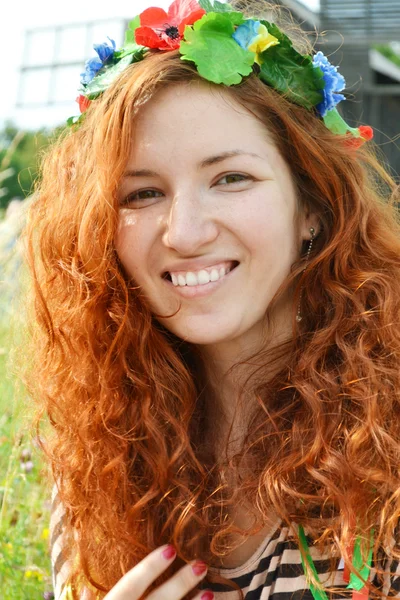 Vakker ung rødhåret med blomster i håret, kvinne som smiler lykkelig med en mølle i bakgrunnen. – stockfoto