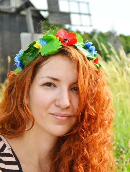 Belle jeune rousse avec des fleurs dans ses cheveux femme souriant joyeusement avec un moulin à l'arrière-plan — Photo