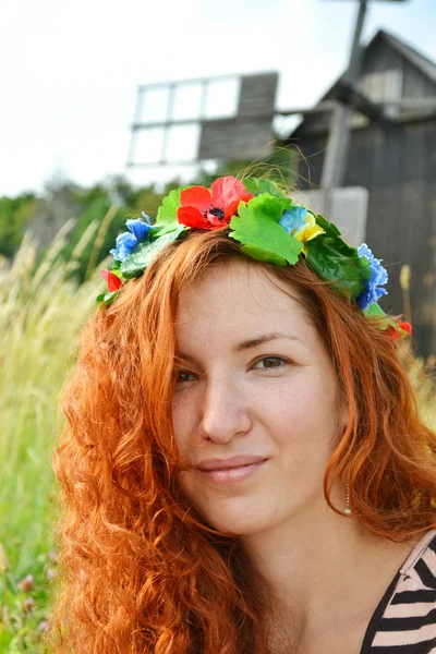 Belle jeune rousse avec des fleurs dans ses cheveux femme souriant joyeusement avec un moulin à l'arrière-plan — Photo