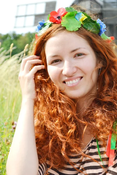 Belle jeune rousse avec des fleurs dans ses cheveux femme souriant joyeusement avec un moulin à l'arrière-plan — Photo