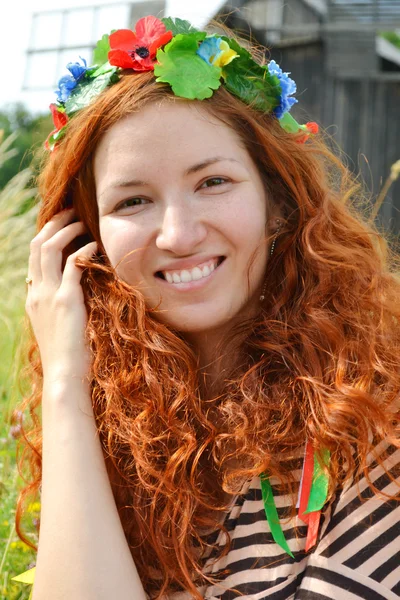 Belle jeune rousse avec des fleurs dans ses cheveux femme souriant joyeusement avec un moulin à l'arrière-plan — Photo