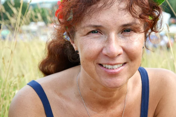 Mujer pelirroja hermosa feliz con flores en el pelo en sus cuarentas oliendo al aire libre — Foto de Stock