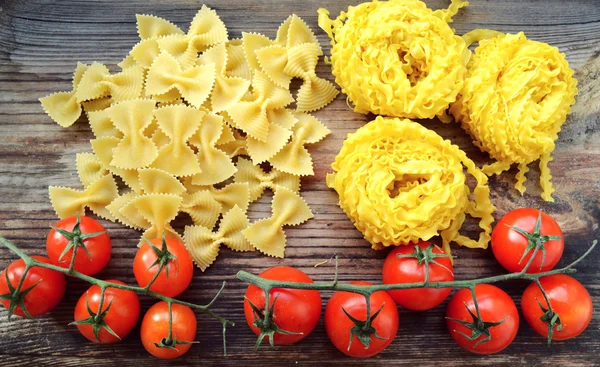 Mazzo di pomodorini rossi con pasta cruda Reginette (Mafaldine) e farfalle di pasta a forma di farfalla sul tavolo di legno — Foto Stock