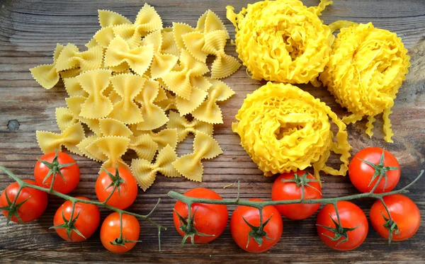 Bando de pequenos tomates cereja vermelha com macarrão cru Reginette (Mafaldine) e borboleta em forma de farfalle macarrão na mesa de madeira — Fotografia de Stock