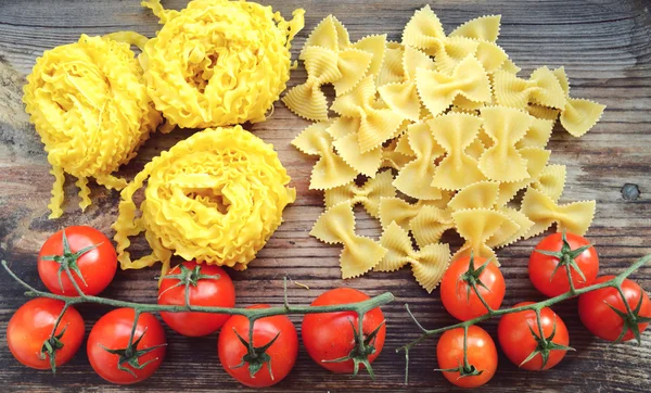 Bando de pequenos tomates cereja vermelha com macarrão cru Reginette (Mafaldine) e borboleta em forma de farfalle macarrão na mesa de madeira — Fotografia de Stock