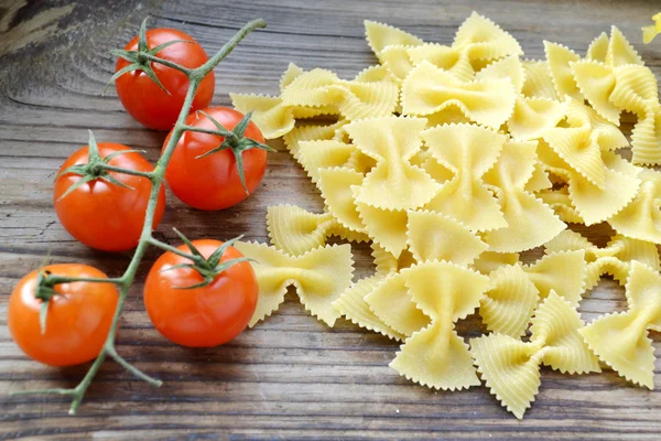 Mazzo di pomodorini rossi e farfalle di pasta a forma di farfalle sul tavolo di legno — Foto Stock